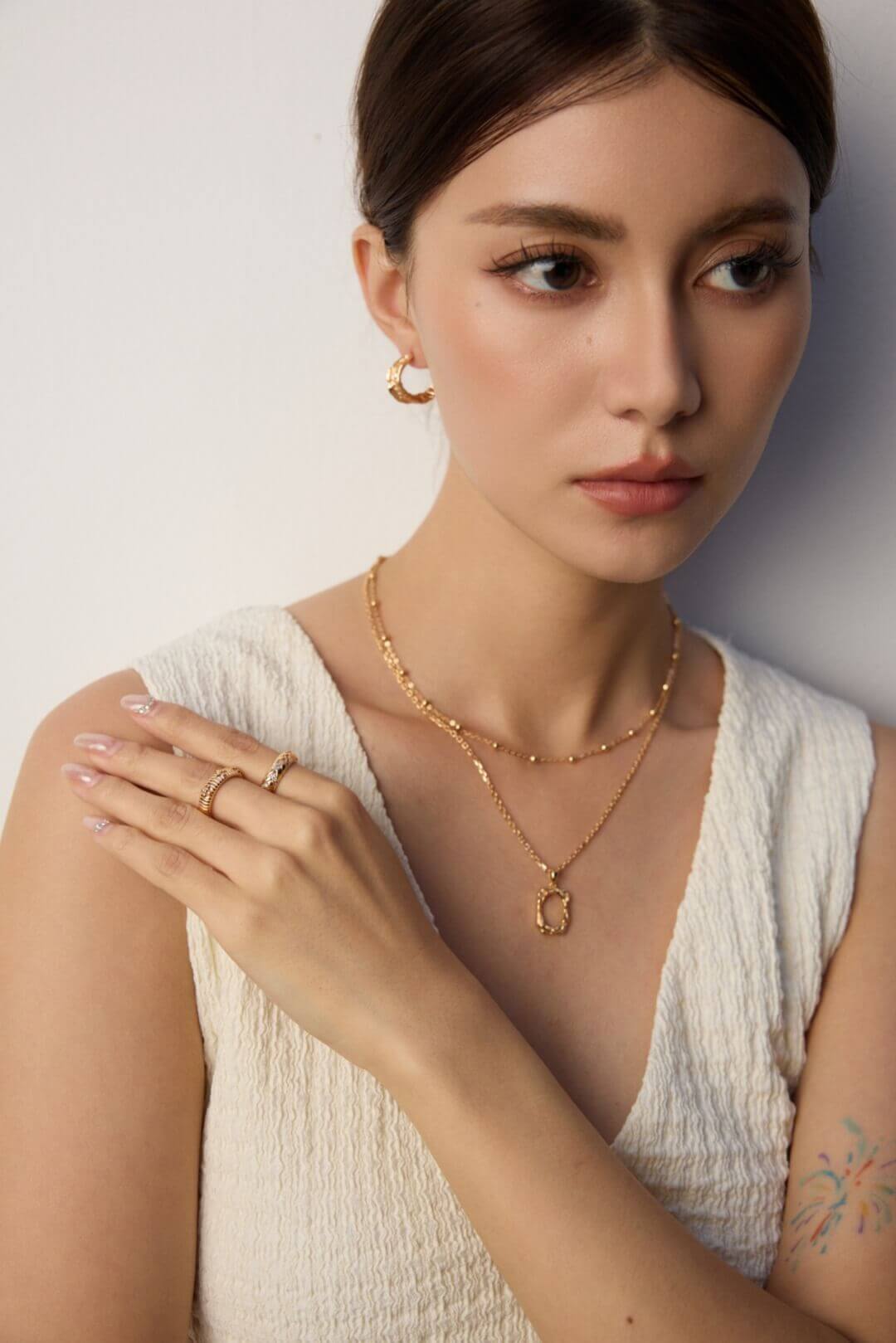 Woman wearing gold jewelry against a neutral background