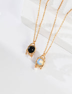 Two gold necklaces with gemstone pendants on a white surface