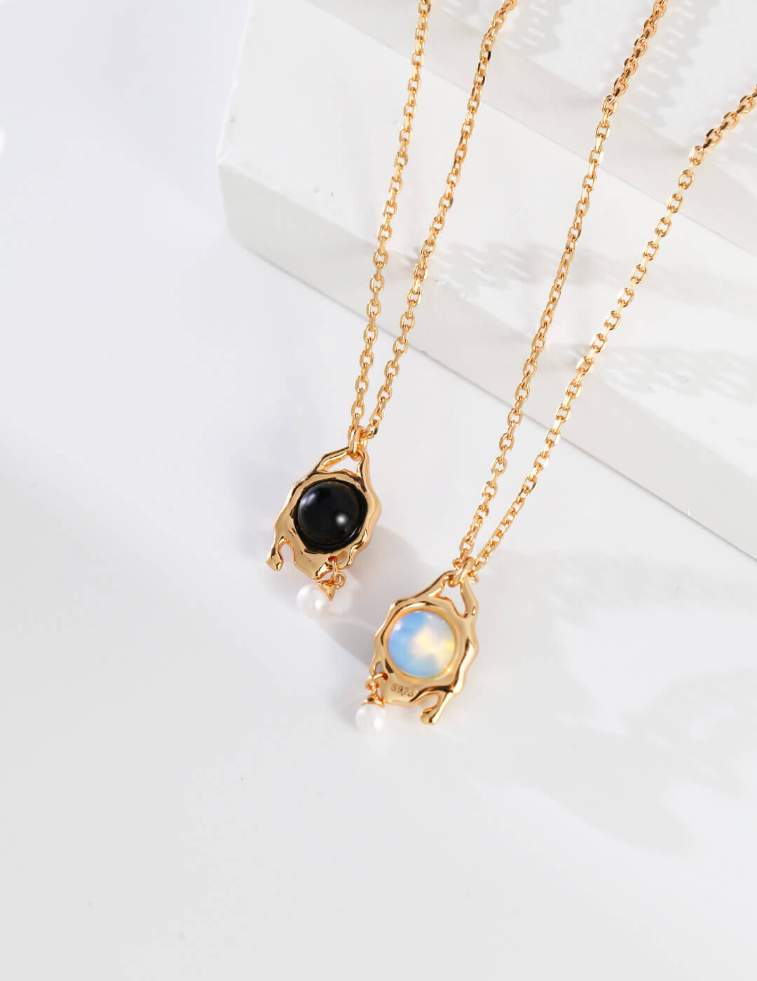 Two gold necklaces with gemstone pendants on a white surface