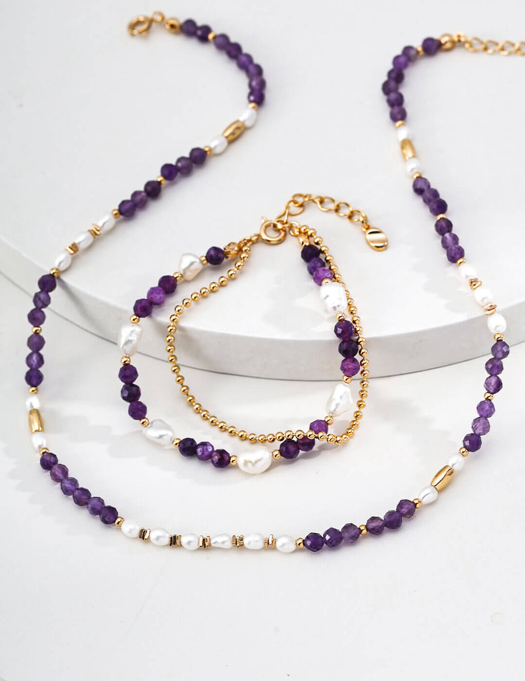Set of purple beaded necklaces and bracelets on a white surface