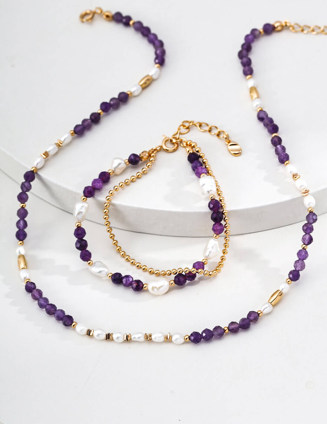 Set of purple beaded necklaces and bracelets on a white surface