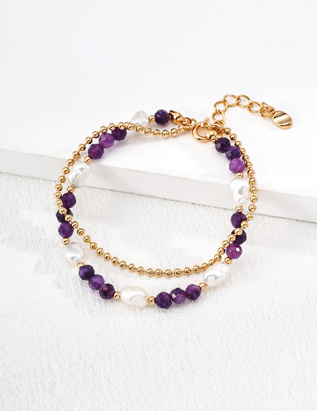 Two-layered bracelet with purple beads and gold chain on a white background