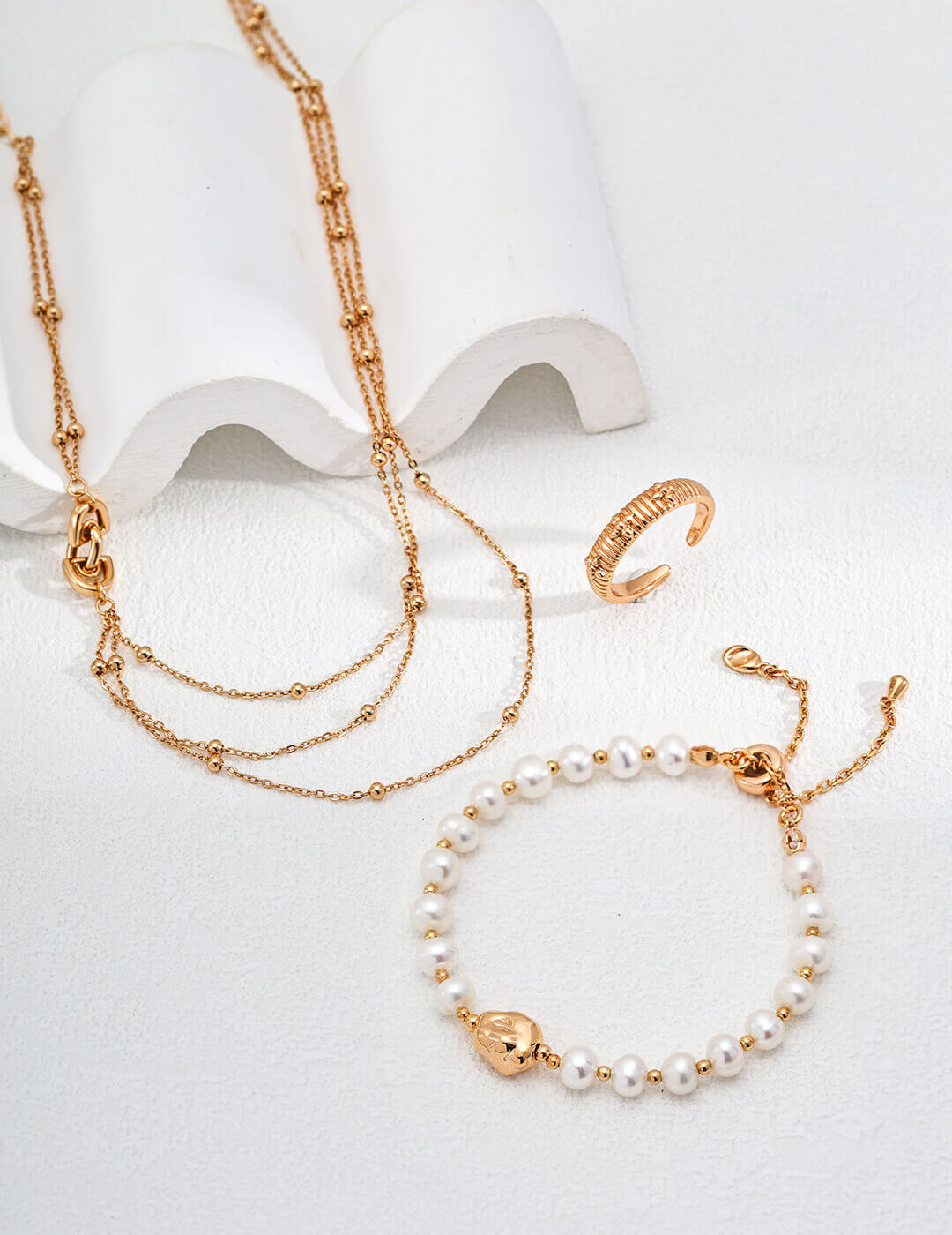 Gold necklace and bracelet with pearl accents on a white background