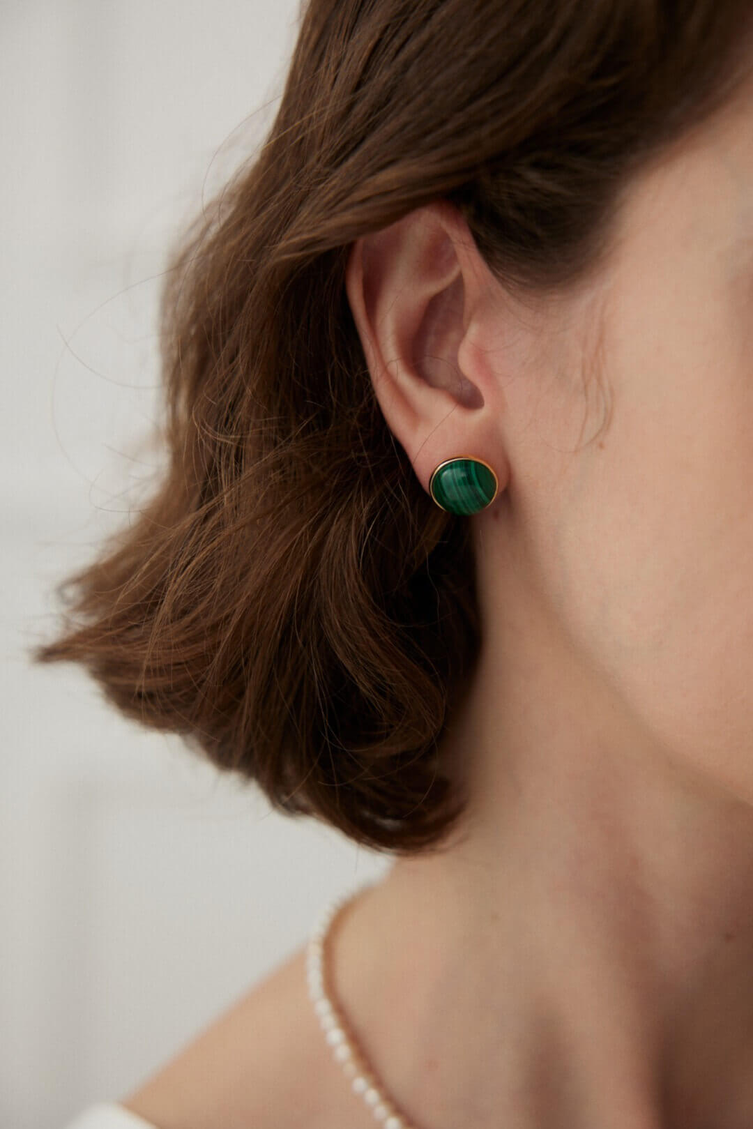 Close-up side view of a woman wearing the green malachite stud earrings, highlighting their subtle elegance against the skin.