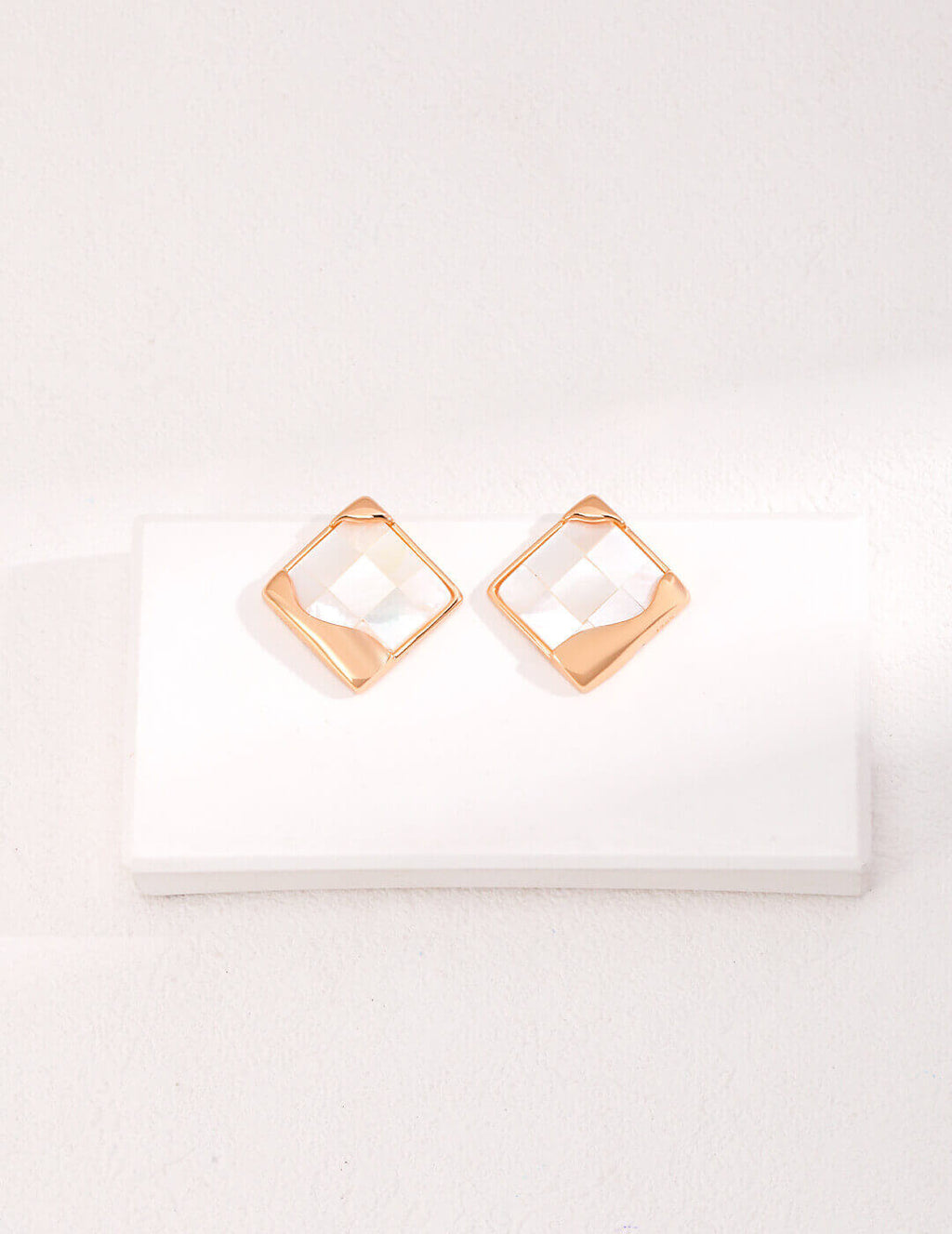 Detailed close-up of intricate mosaic inlay work on white shell earrings, showcasing geometric patterns.
