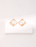 Detailed close-up of intricate mosaic inlay work on white shell earrings, showcasing geometric patterns.