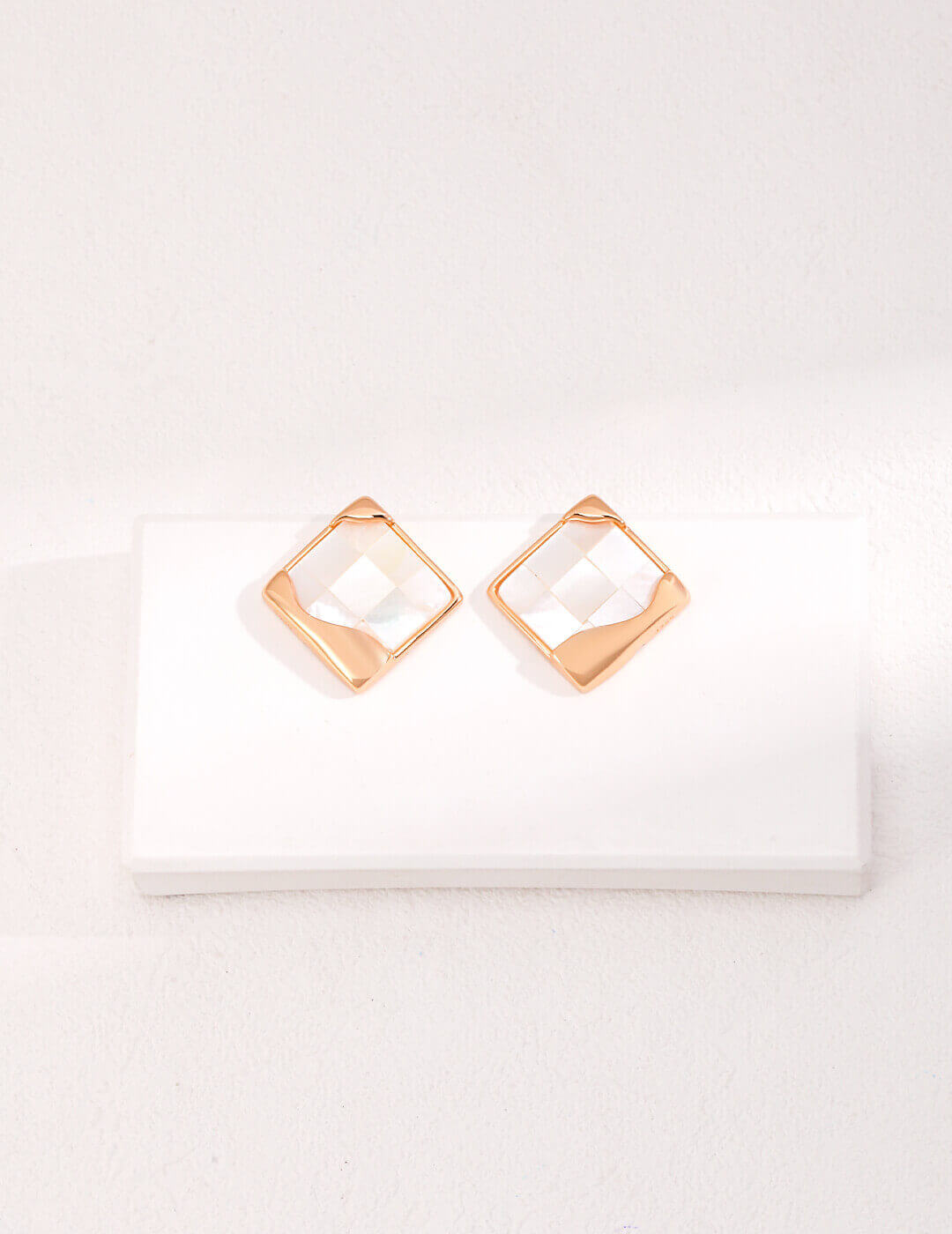 Detailed close-up of intricate mosaic inlay work on white shell earrings, showcasing geometric patterns.