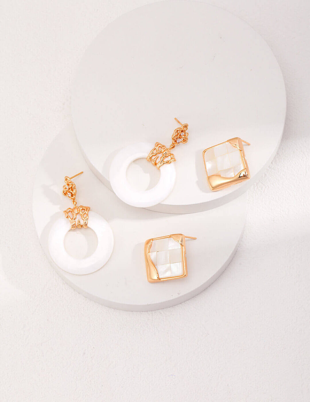 Delicate white shell stud earrings with hollow-out design shown on a fingertip, demonstrating their perfect petite size.
