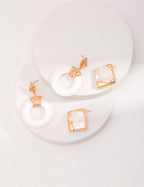 Delicate white shell stud earrings with hollow-out design shown on a fingertip, demonstrating their perfect petite size.