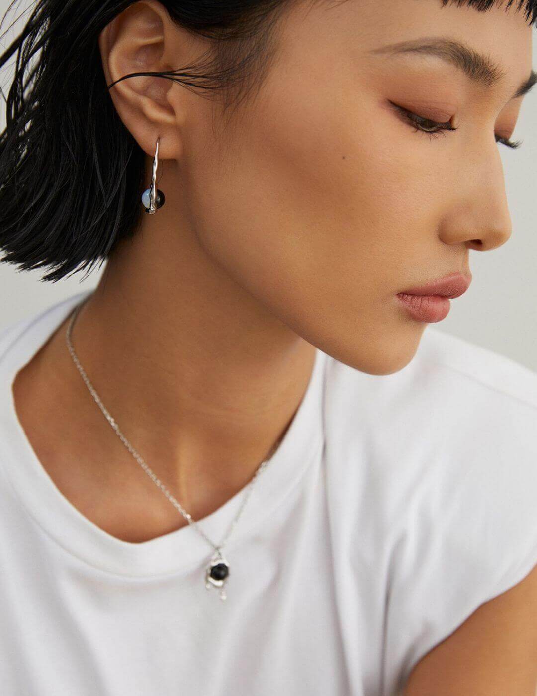Close-up of a person wearing a silver necklace with a black pendant on a plain background