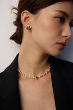 Close-up of a woman wearing a pearl necklace and gold earrings against a neutral background
