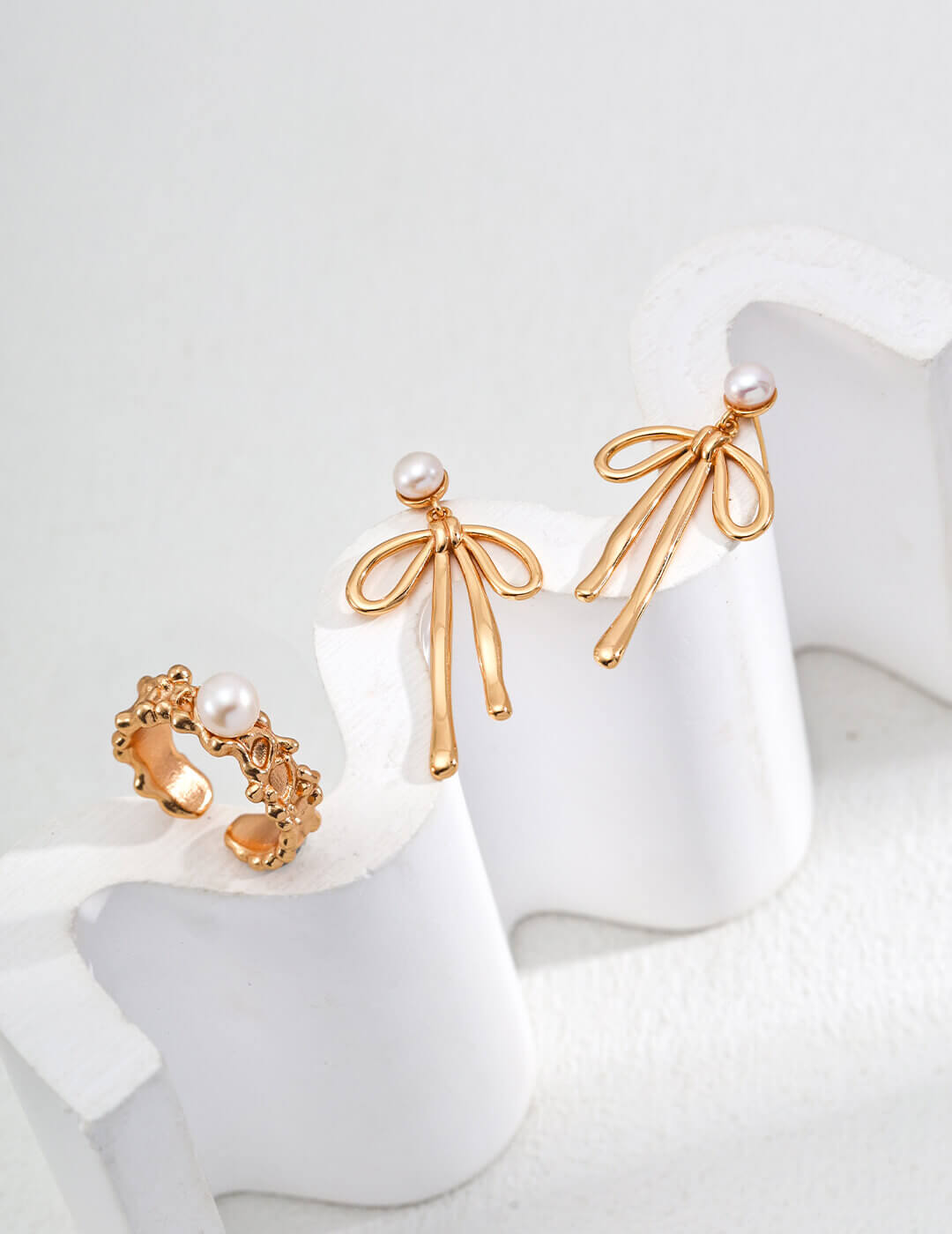 Gold bow-shaped earrings with pearl accents on a white background