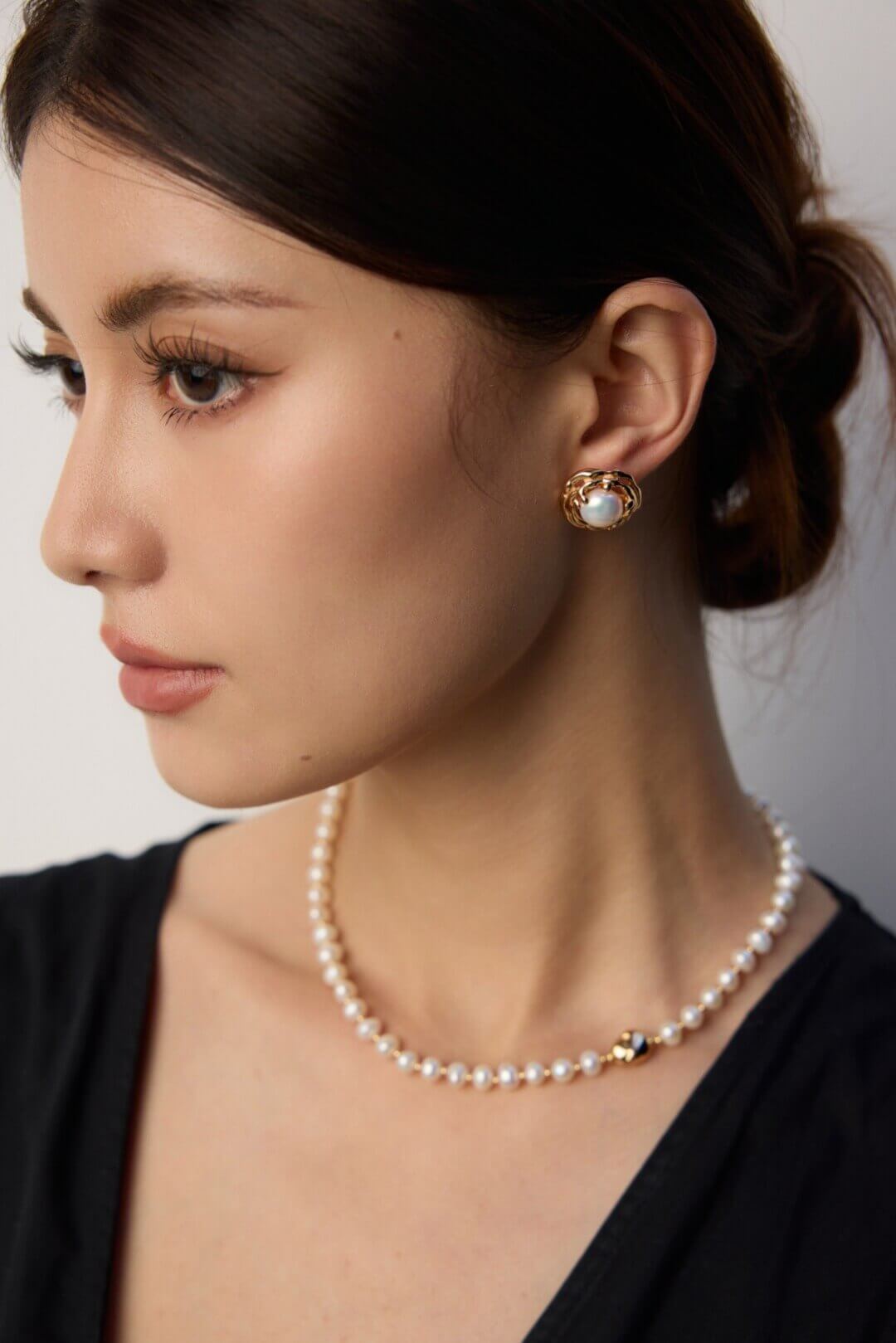 Close-up of a woman wearing pearl earrings and a necklace against a neutral background