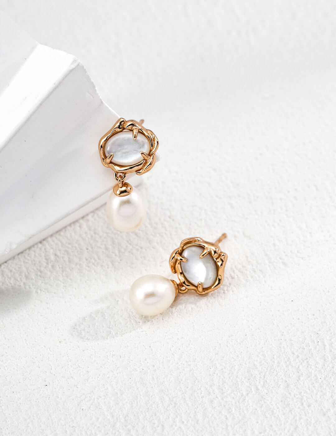 Pair of gold earrings with pearl drops on a white surface