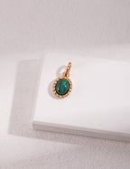 Gold pendant with a green gemstone on a white box