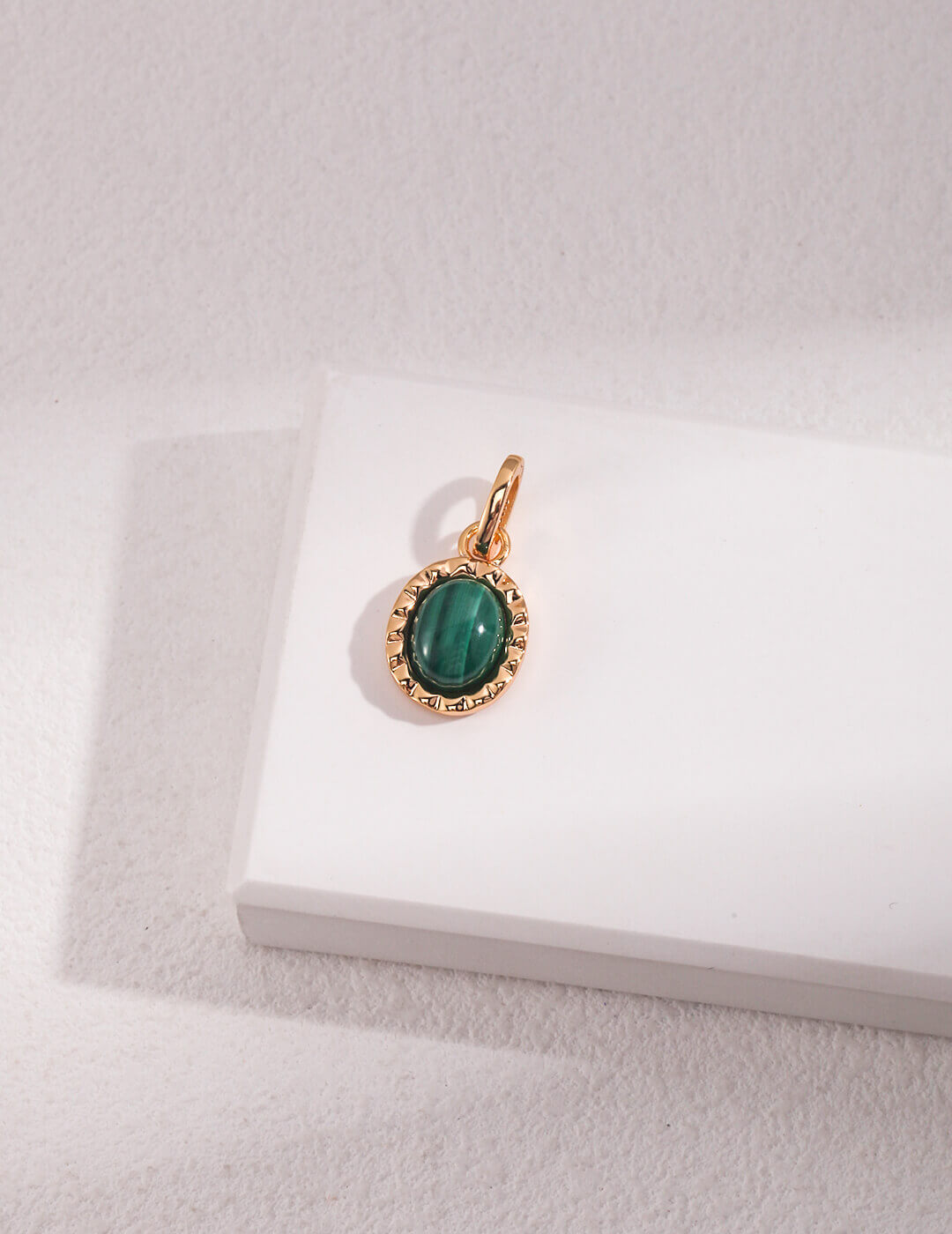 Gold pendant with a green gemstone on a white box