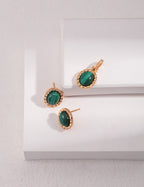 Gold earrings with green gemstones on a white surface