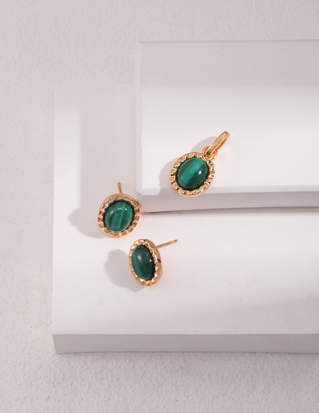 Gold earrings with green gemstones on a white surface