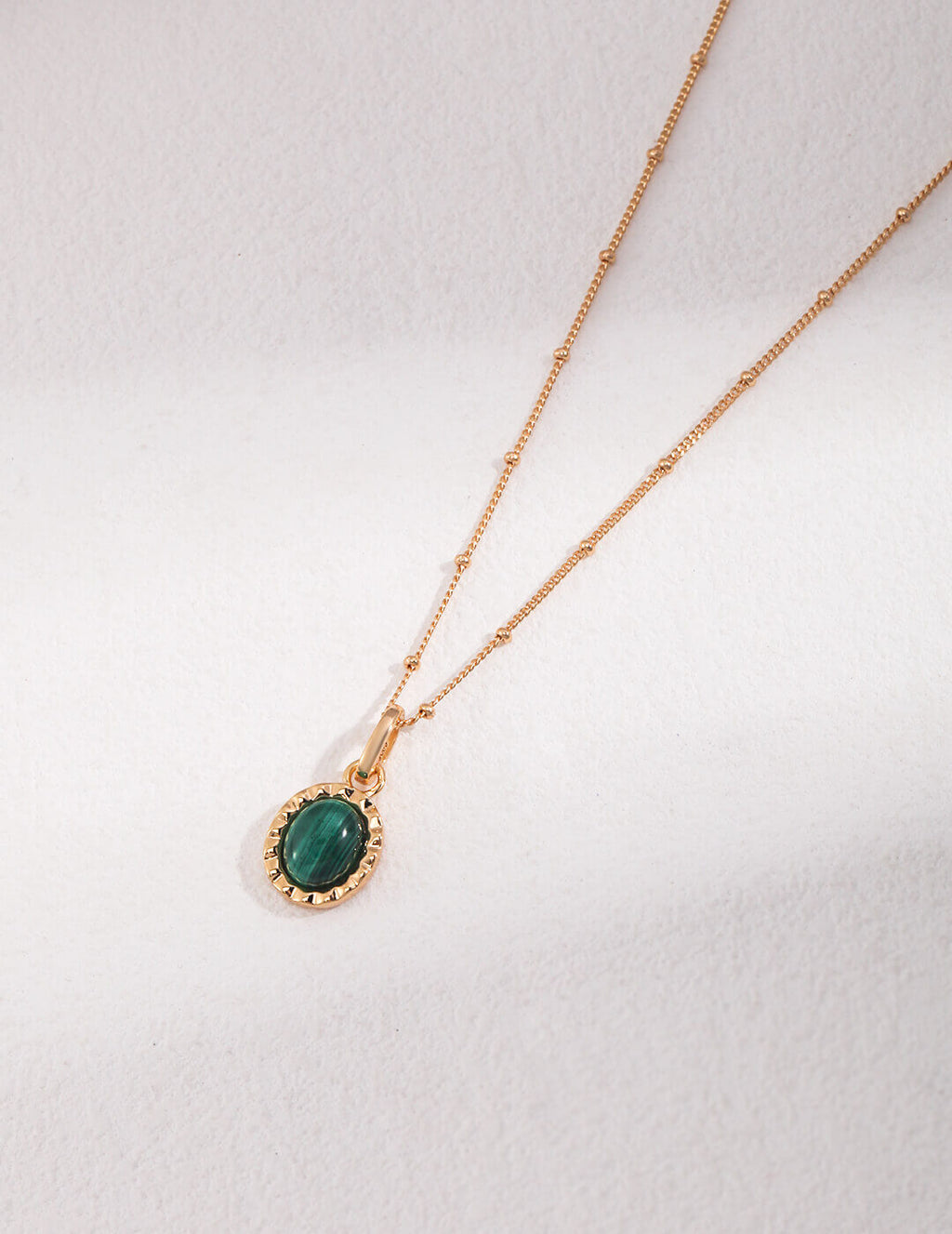 Gold necklace with a green gemstone pendant on a white background