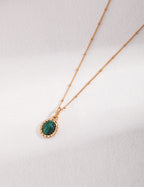 Gold necklace with a green gemstone pendant on a white background
