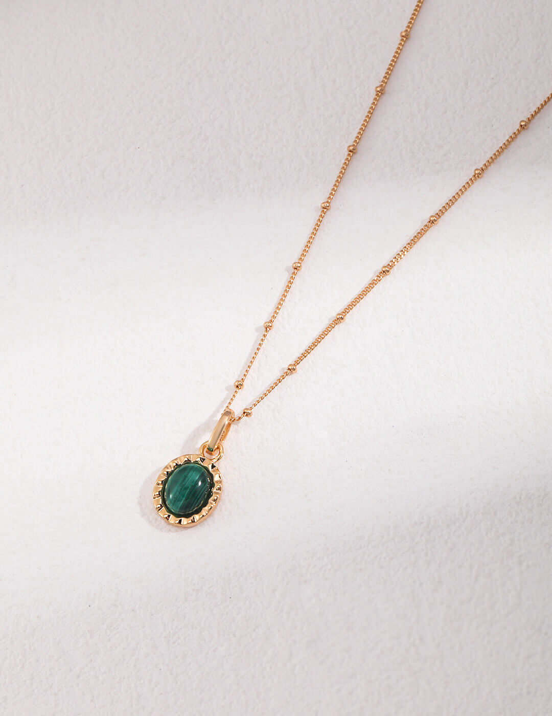 Gold necklace with a green gemstone pendant on a white background