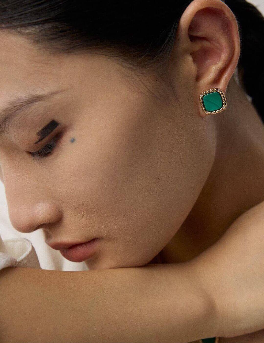 Close-up of a person wearing a green earring with a gold setting.