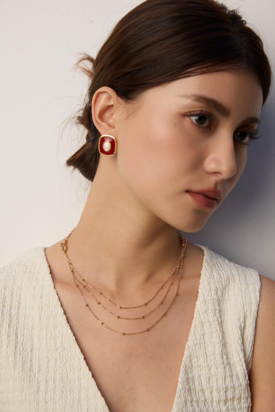 Woman wearing a gold necklace and red earrings against a neutral background