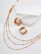 Gold hoop earrings with a gold chain necklace on a white background