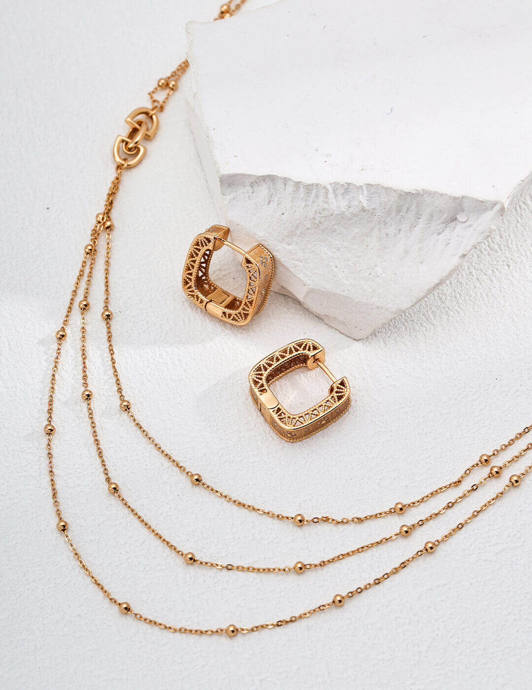 Gold hoop earrings with a gold chain necklace on a white background