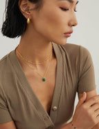 Woman wearing a gold necklace with a green gemstone, looking away from the camera.
