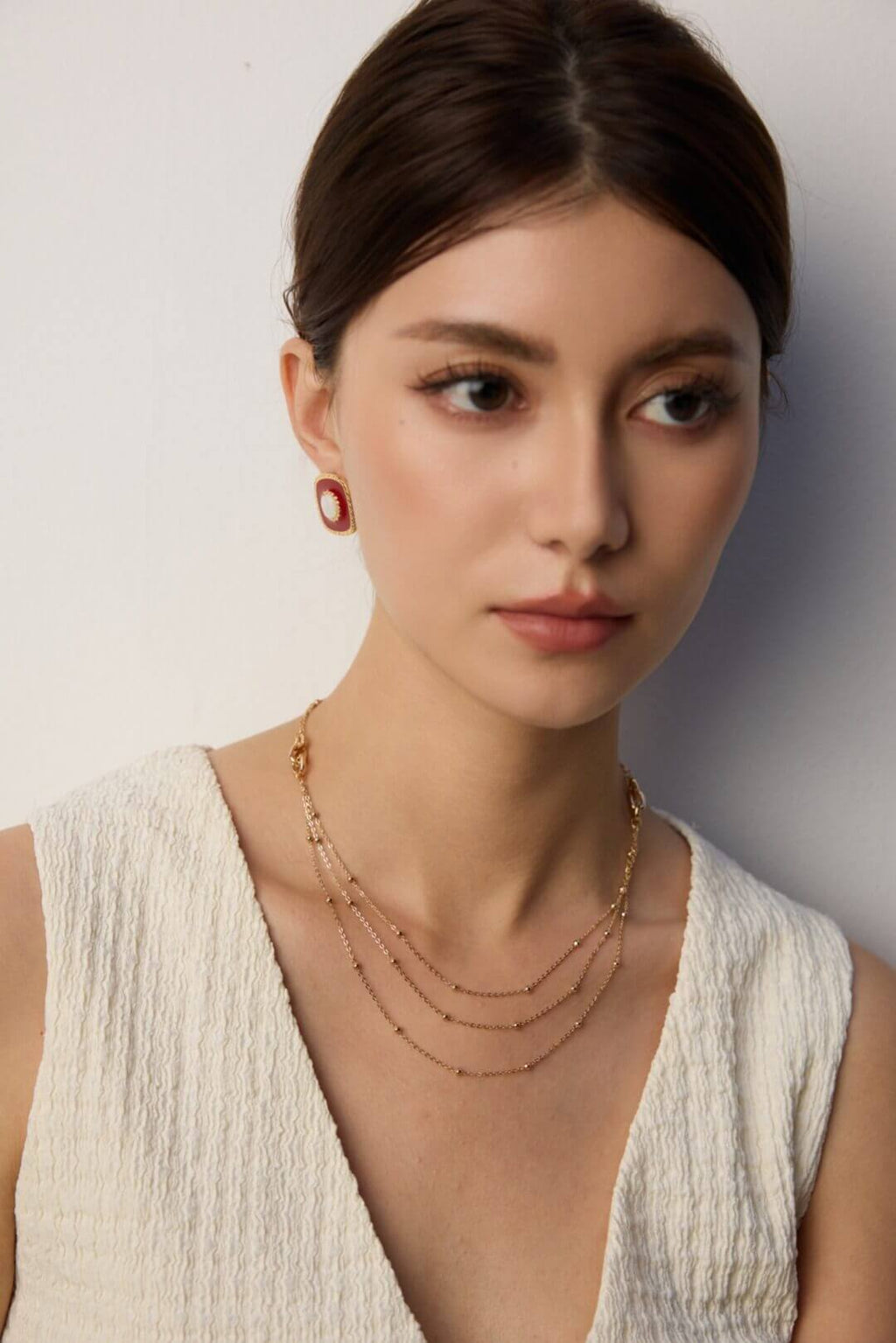 Woman wearing gold necklaces and earrings against a plain background