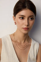 Woman wearing gold necklaces and earrings against a plain background