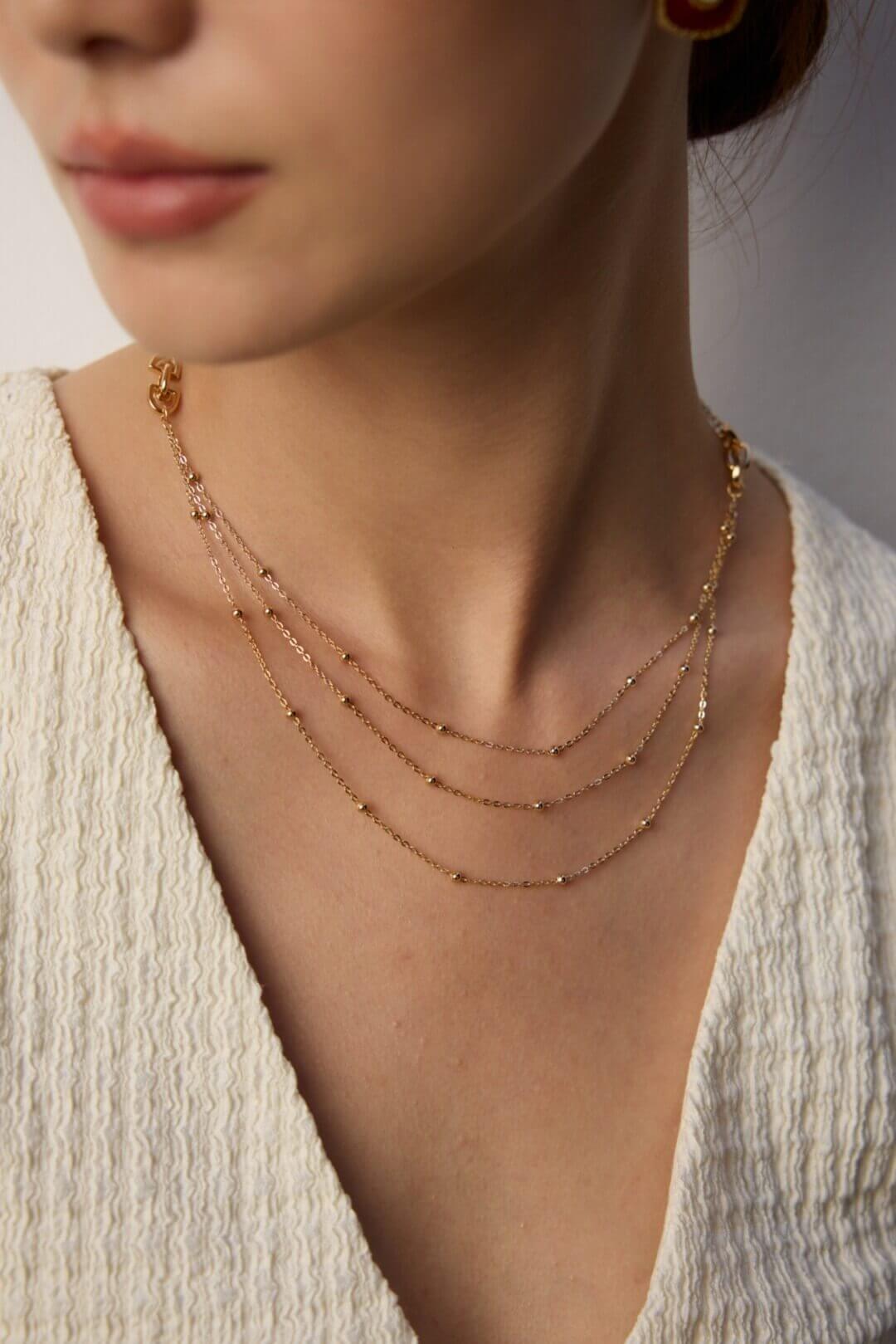 Close-up of a person wearing a delicate gold necklace with a neutral background