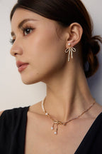 Close-up of a woman wearing gold bow earrings and a matching necklace against a neutral background