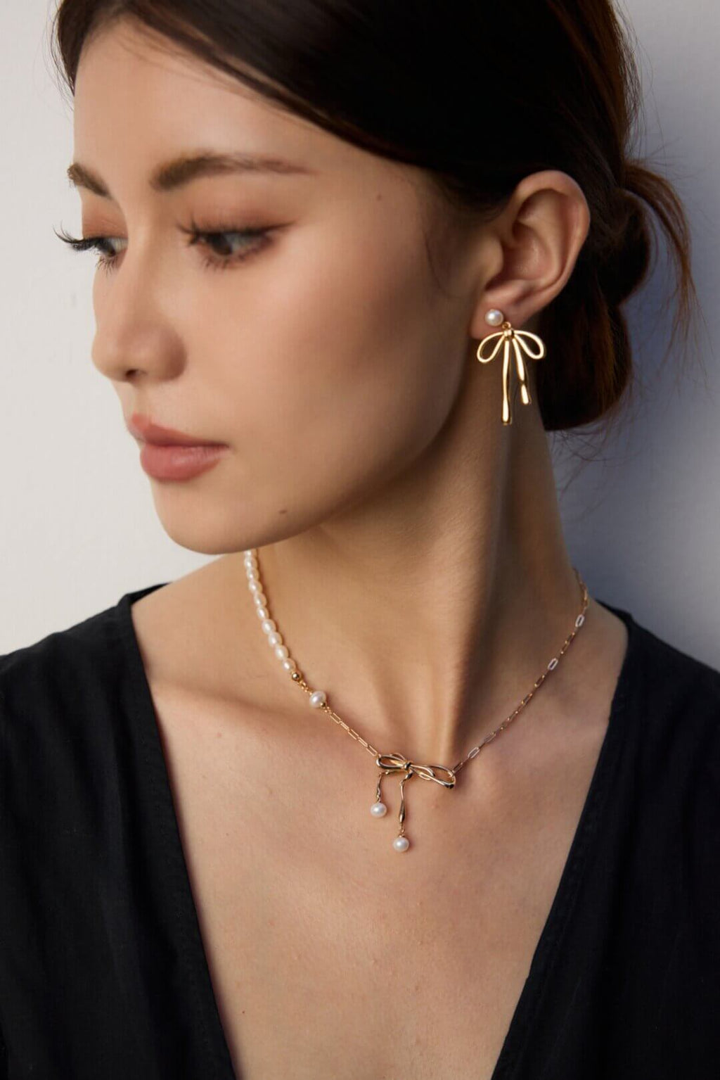 Woman wearing a gold bow earring and necklace against a neutral background