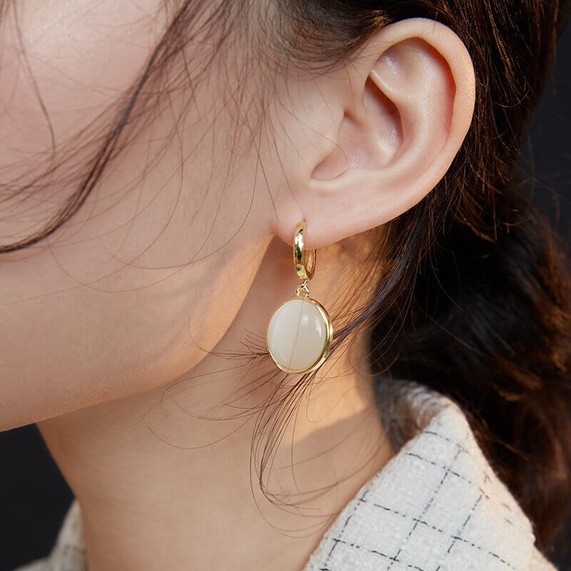 Woman wearing cat's eye earrings in elegant indoor setting.