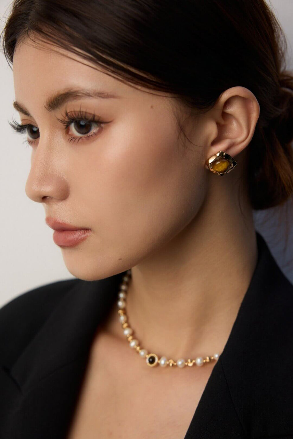 Close-up of a woman wearing a pearl necklace and earring with a neutral background