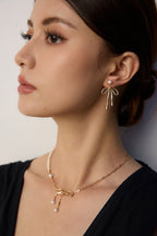 Woman wearing gold bow-shaped earrings and necklace against a neutral background