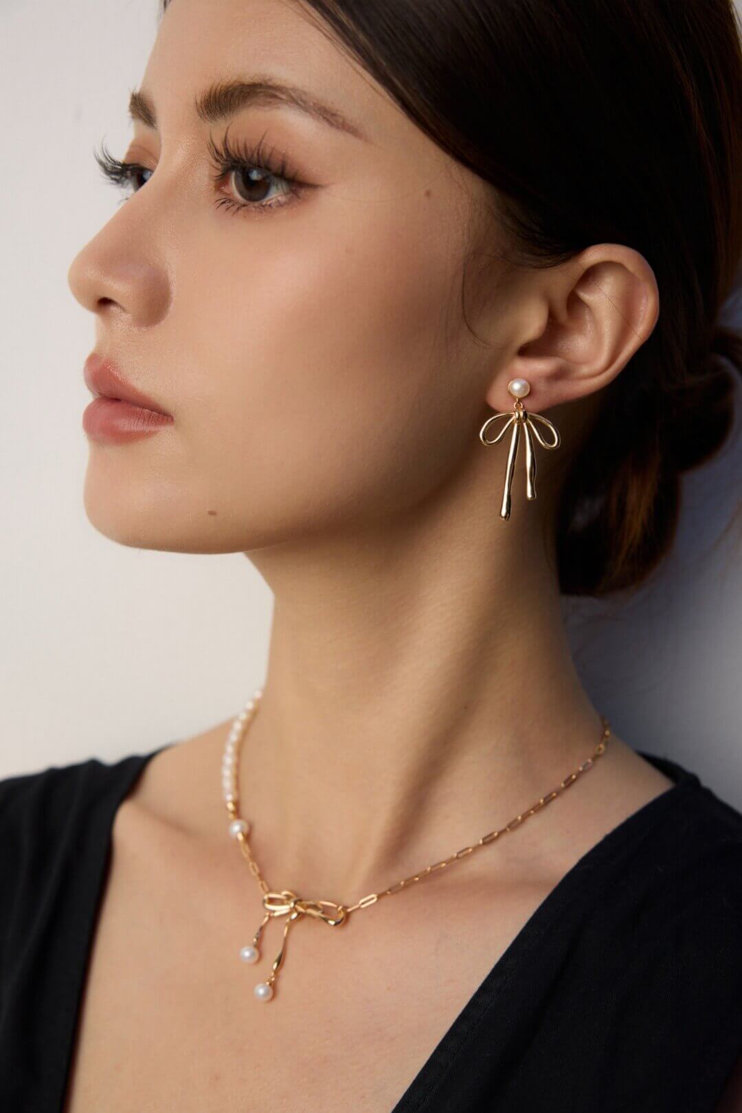 Woman wearing gold bow-shaped earrings and necklace against a neutral background
