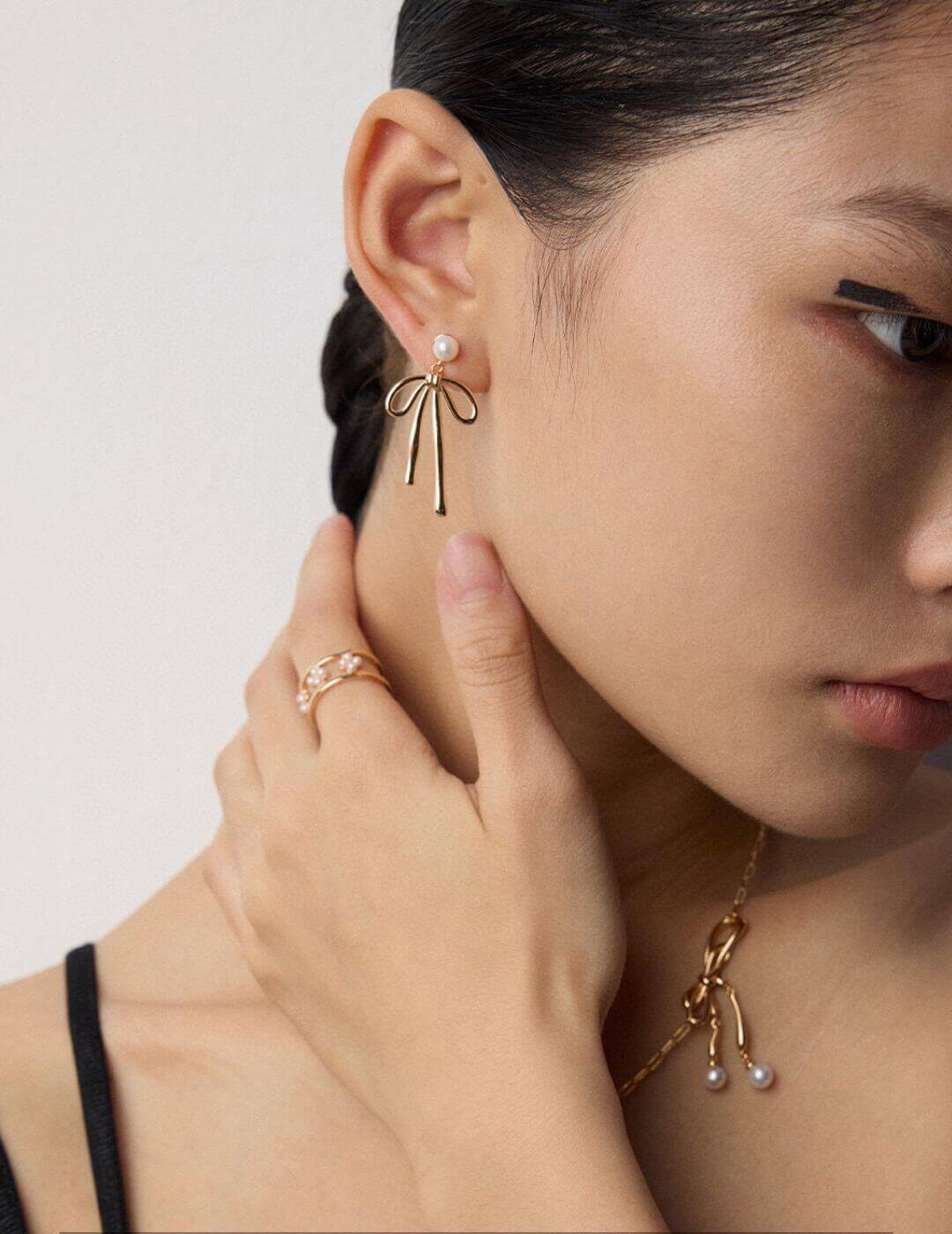 Close-up of a person wearing gold earrings and a necklace with pearl drops on a plain background