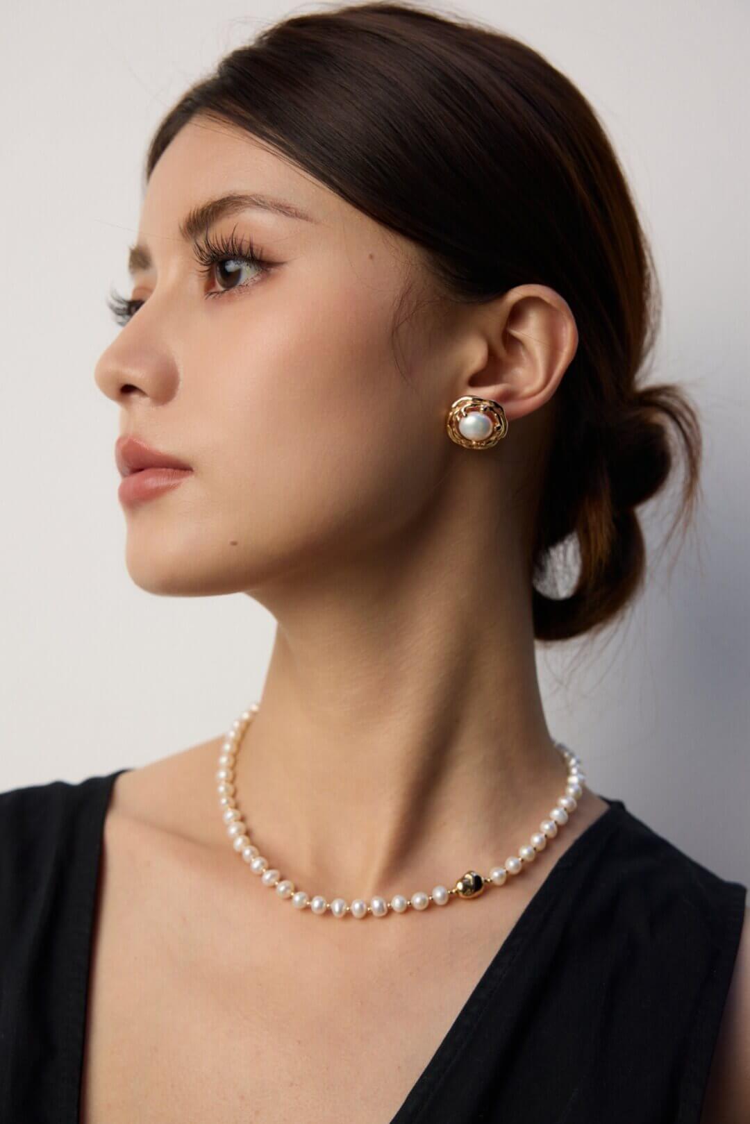 Woman wearing pearl necklace and earrings against a neutral background