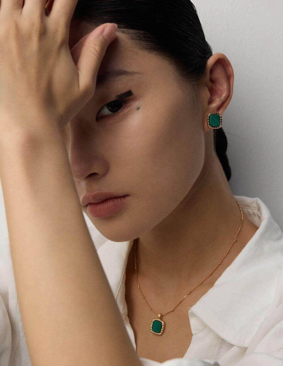 Woman wearing green earrings and a necklace with a plain background