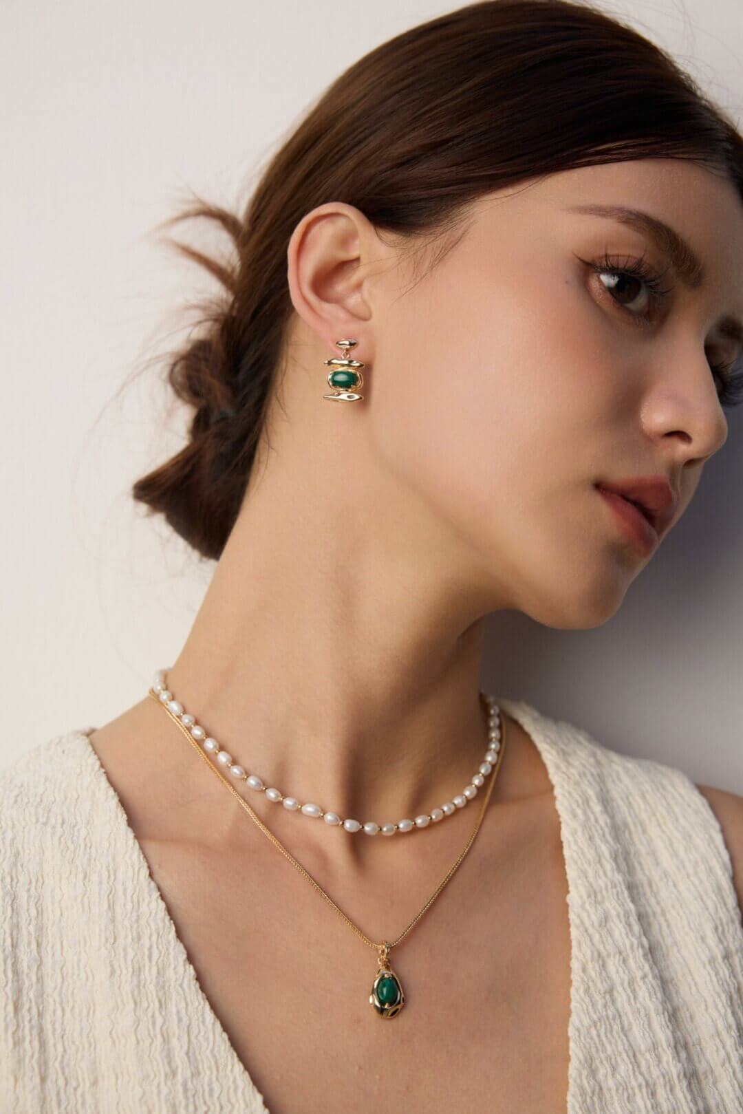 The malachite pendant layered with other gold necklaces on a model.