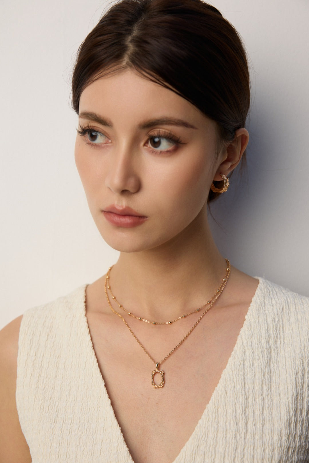 Woman wearing gold jewelry against a neutral background