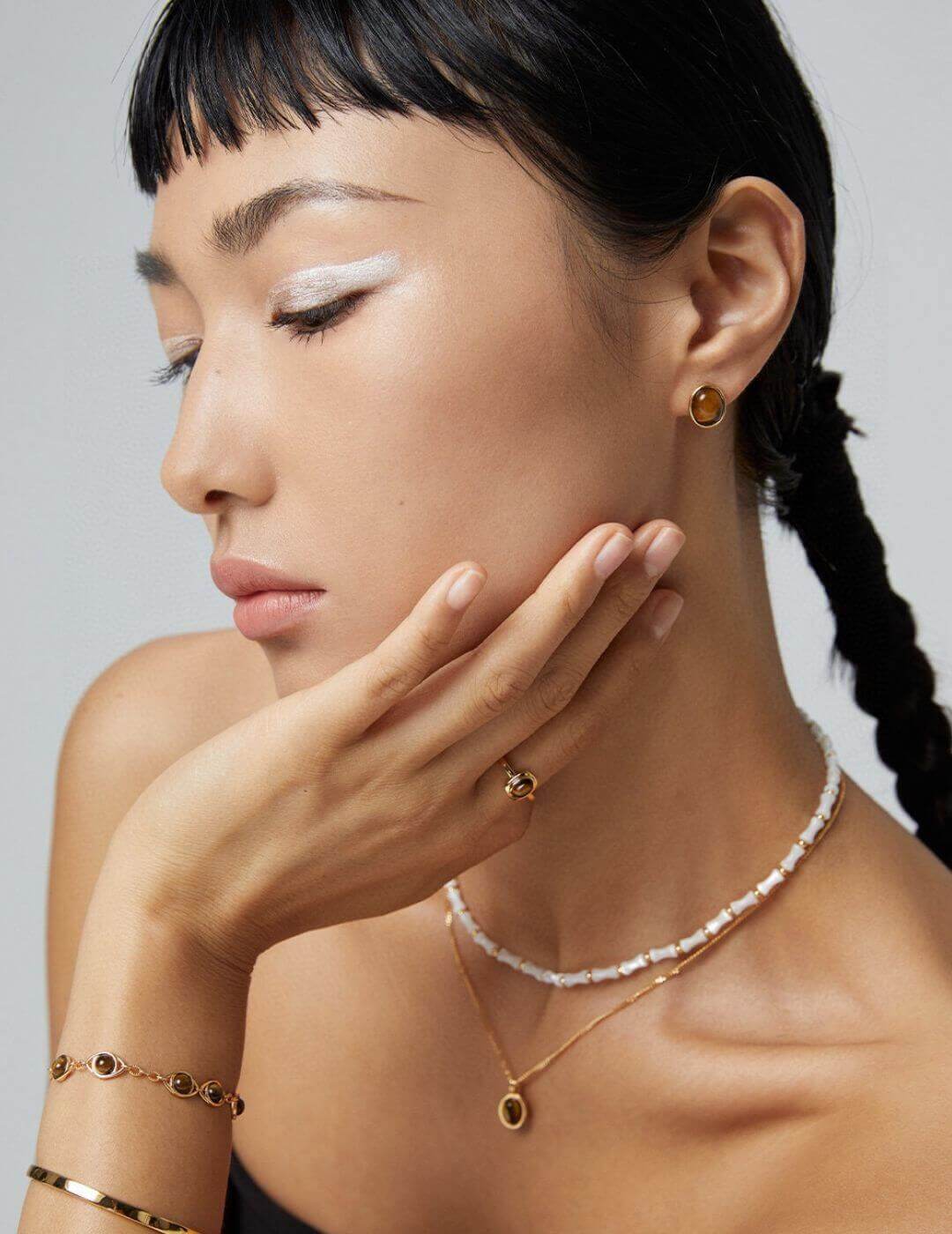 Woman wearing gold jewelry including earrings, necklace, and bracelet against a neutral background