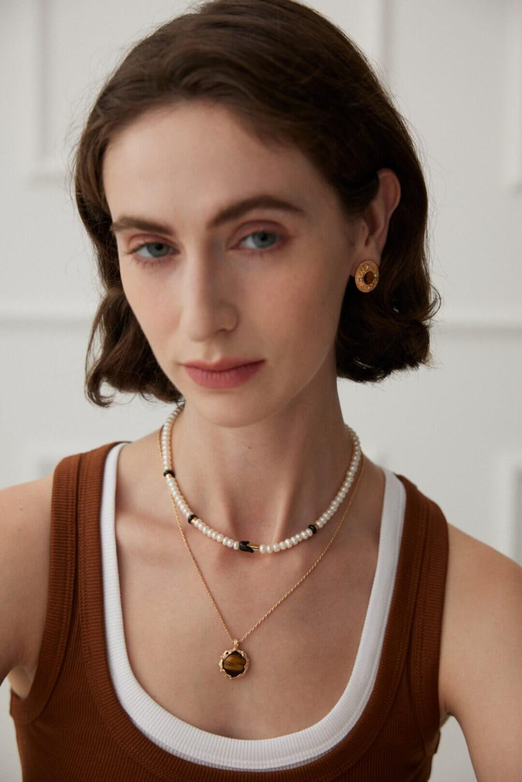 Woman wearing a pearl necklace and gold earrings against a white background