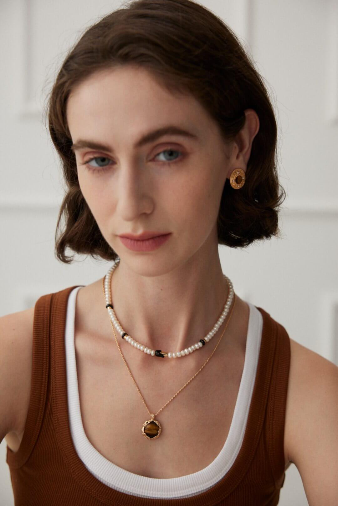 Woman wearing a pearl necklace and gold earrings against a white background