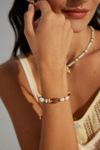 Close-up of a person wearing a gold bracelet with small stones on a neutral background