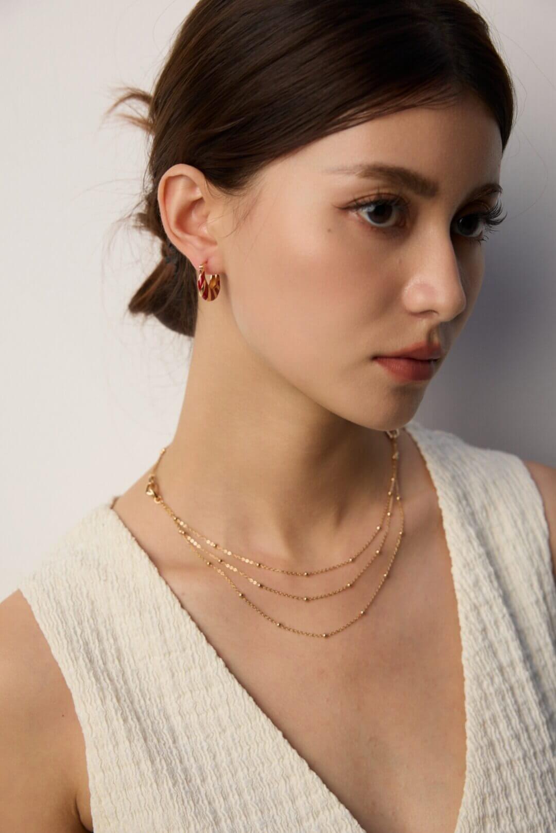 Woman wearing gold necklaces and earrings against a neutral background