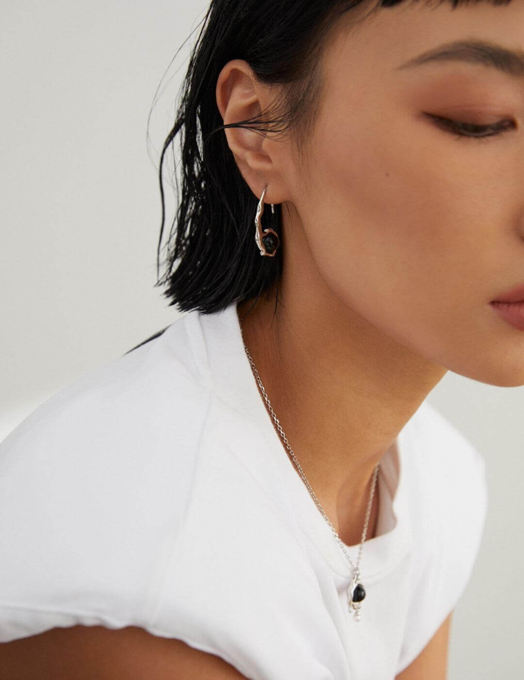 Close-up of a person wearing earrings and a necklace against a neutral background
